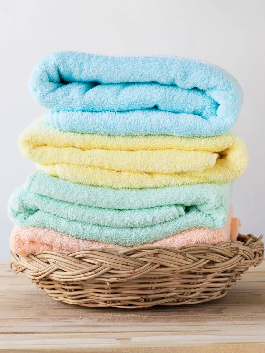 a stack of newly washed towels of multiple colors sitting in a brown basket