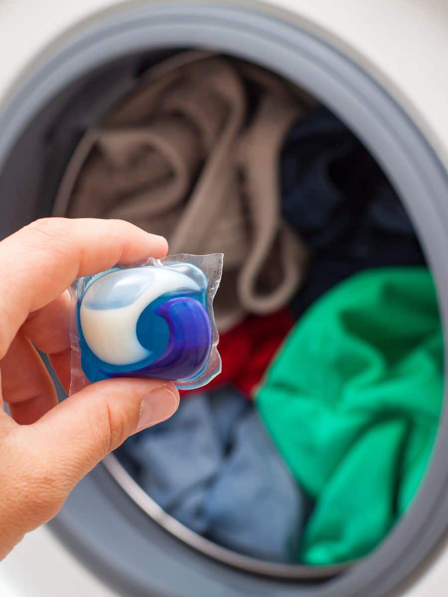 someone putting a laundry detergent pod into the washing machine instead of measuring out laundry detergent