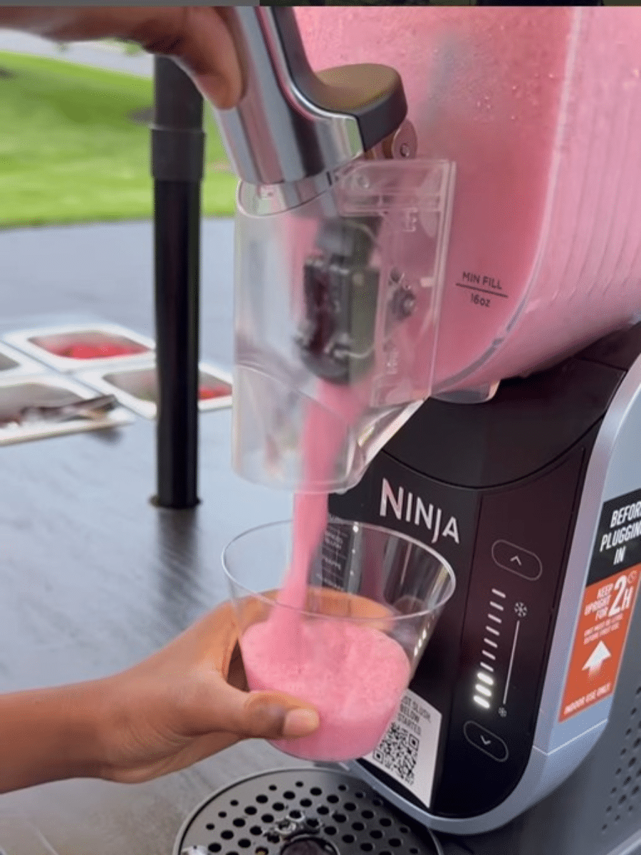 a hand holding a cup that is being filled with pink slushie form the Ninja slushie machine.