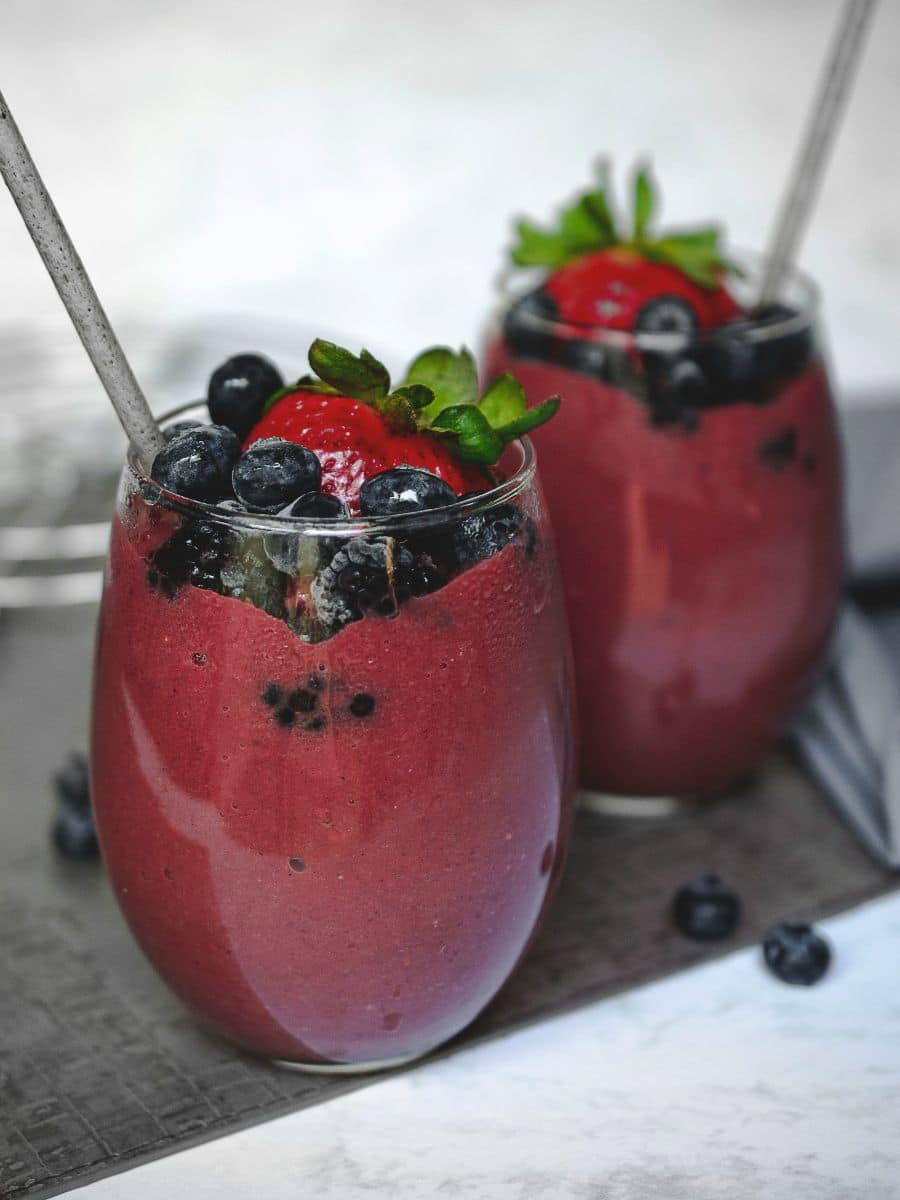 black raspberry kool aid slushie's made in a blender with fruit on top and a straw in them.