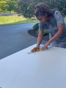 A woman using a ruler and pencil to make an outline on a piece of wood.