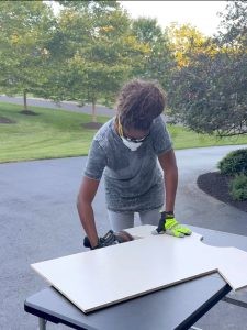 a woman using a sander to sand the edges of a piece of wood shaped as a jersey.