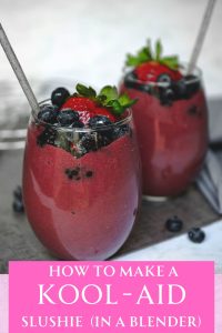 two glasses filled with purple slushie with fruit on top and a straw sticking out.