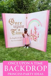 Once upon a time story book prop with a little girl in a pink dress standing in front of it in the grass.