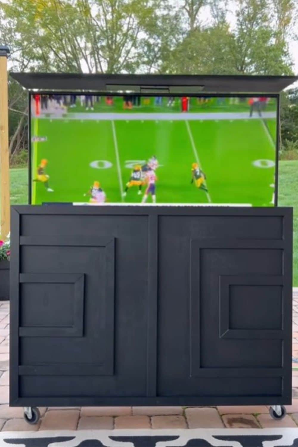 A TV playing a football game coming out of a black cabinet with black trim on a patio.