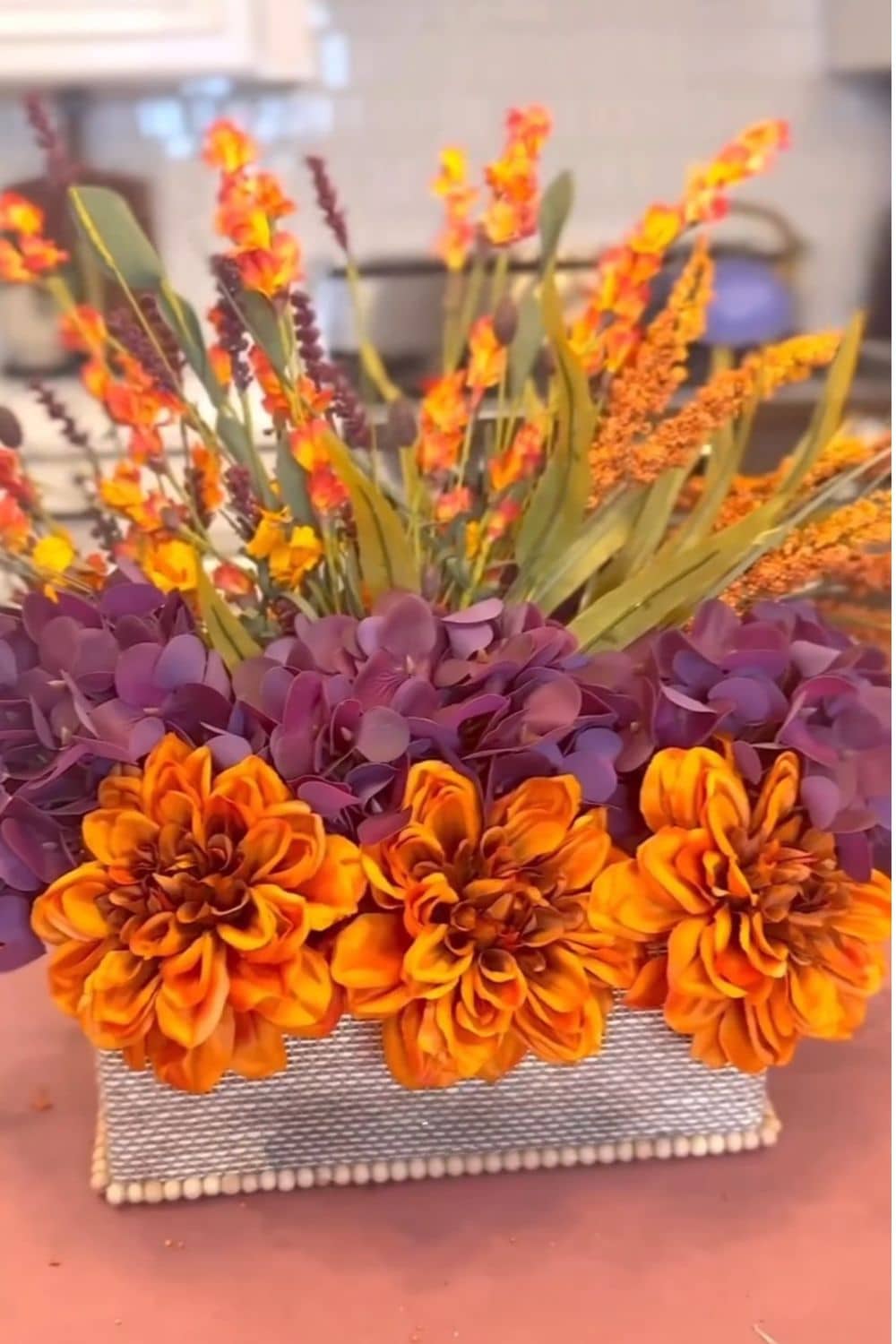 A fall flower arrangement in a grass cloth covered box with wooden beads around the edges.