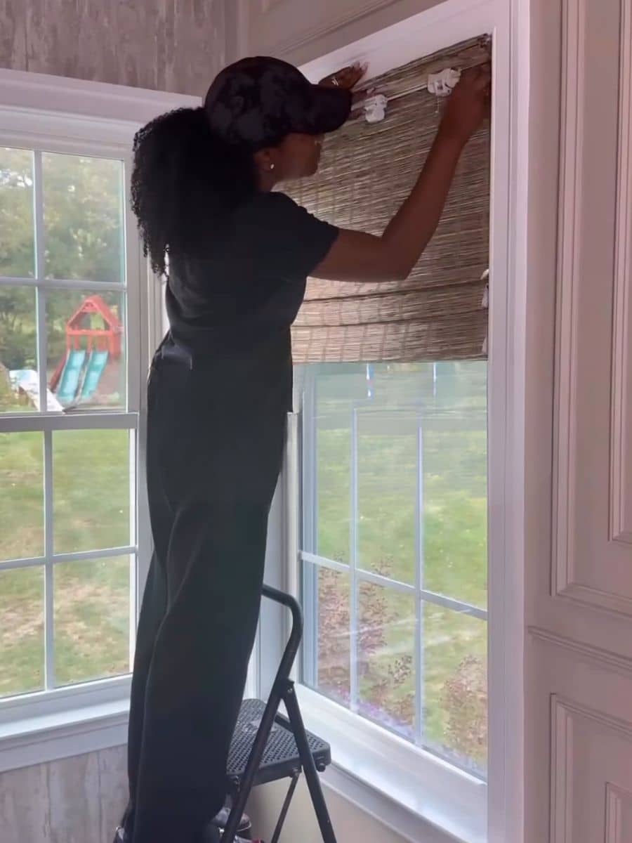 A woman installing woven shades on a window.